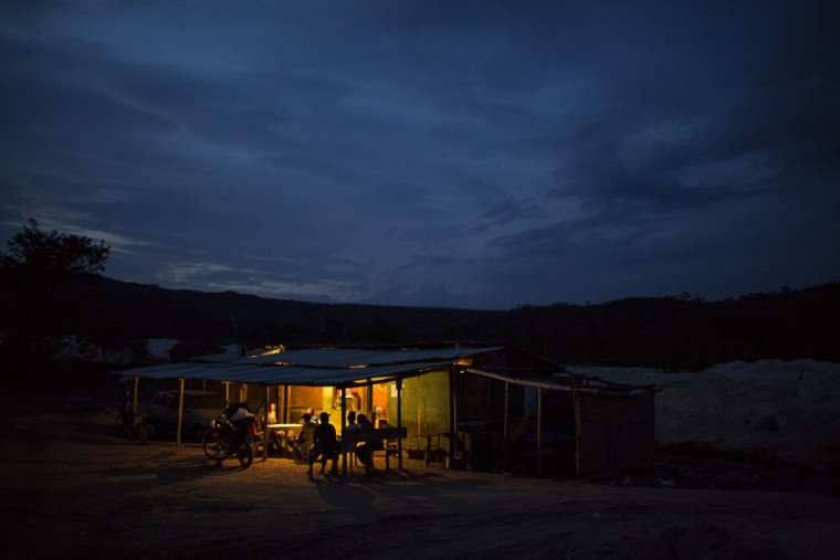 In this Nov. 17, 2015 photo, artisanal diamond miners gather inside a bar kept lit at dusk by a generator in Areinha, Minas Gerais state, Brazil. The rural miners live in wooden huts without electricity and bathe with water in buckets, barely surviving without a stable income but on rare occasions enjoying a windfall of tens of thousands of dollars. (AP Photo/Felipe Dana)