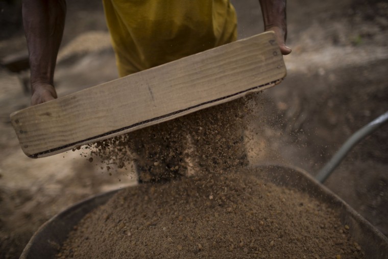 In this Nov. 14, 2015 photo, an artisanal miner separates rocks gathered from a crater left behind by giant diamond mining companies in Areinha, Minas Gerais state, Brazil. Today the devastated area known as Areinha is a no manís land where small groups of rural miners try their luck with artisan techniques, using wooden knives, metal pans, large water pumps and no infrastructure. (AP Photo/Felipe Dana)