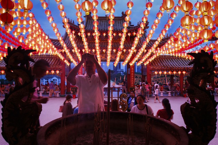 A Malaysian ethnic Chinese man offer prayers under the illuminated traditional Chinese lanterns on the eve of Lunar New Year in Kuala Lumpur, Malaysia, Sunday, Feb. 7, 2016. The Lunar New Year which falls on Feb. 8 this year marks the Year of the Monkey in the Chinese calendar. (AP Photo/Joshua Paul)