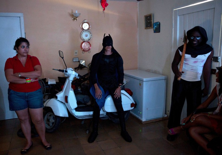 A young man dressed as Batman waits atop a Vespa scooter, stored in the living room of a home at the start of a Halloween party in Havana, Cuba, Friday, Oct. 28, 2016. Marta Perez, left, will be supervising the teen party, which her son is attending. (AP Photo/Ramon Espinosa)